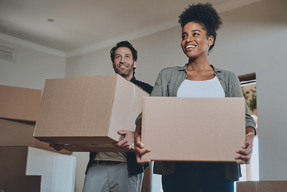 Image of a man and woman carrying boxes through a house.