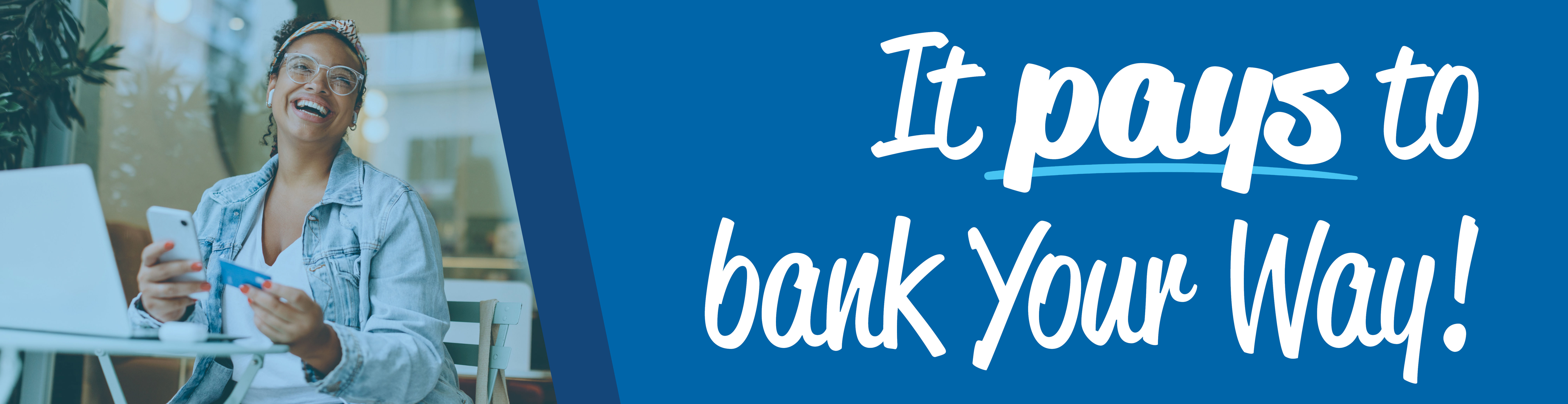 An image of a woman sitting at a table in front of a laptop holing a cellphone and debit card looking off to the right with a big smile. To the right of her is white words over a dark blue shape that says "It pays to bank Your Way!"